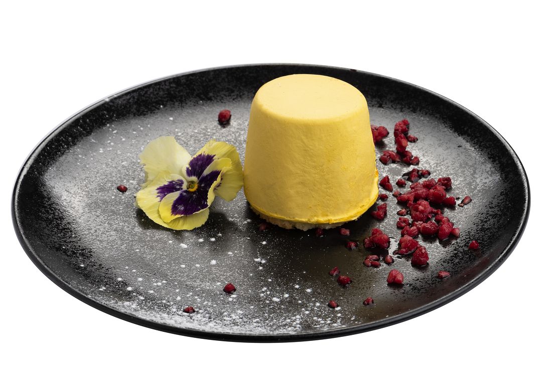 Mango dessert on a dark plate with edible flower, food photography Singapore